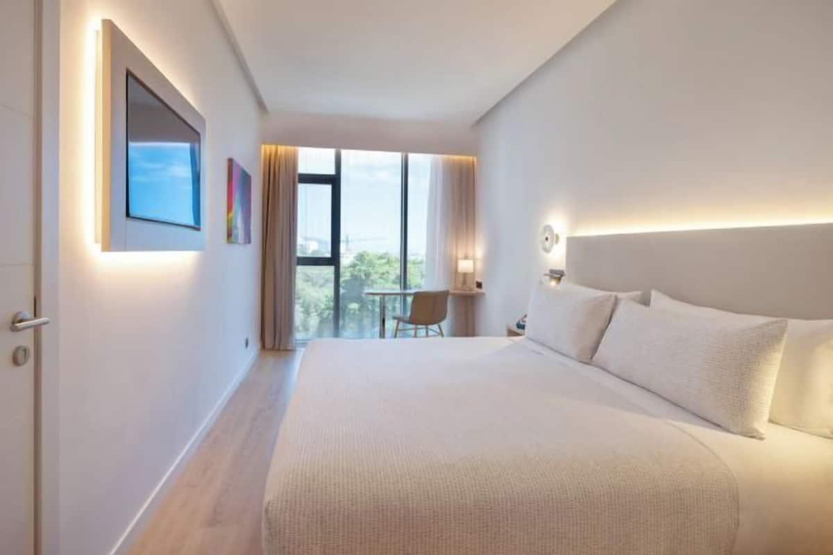 Ein modernes Hotelzimmer mit einem großen Bett, einem Schreibtisch und Blick ins Freie.