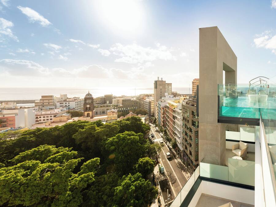 Um edifício alto com piscina infinita de vidro e vista para a cidade e o mar.