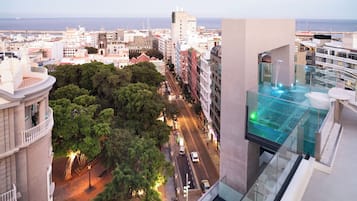 Un hotel alt amb piscina d'infinity a la terrassa, vistes a la ciutat i un carrer animat a baix.