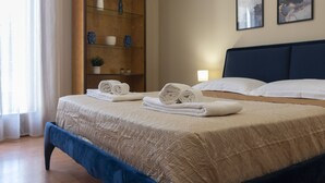 Una cama bien hecha con toallas enrolladas, un estante de madera con adornos y dos cuadros en la pared.