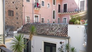 Un patio con techo de tejas, pared de piedra y edificio rosa con balcones.