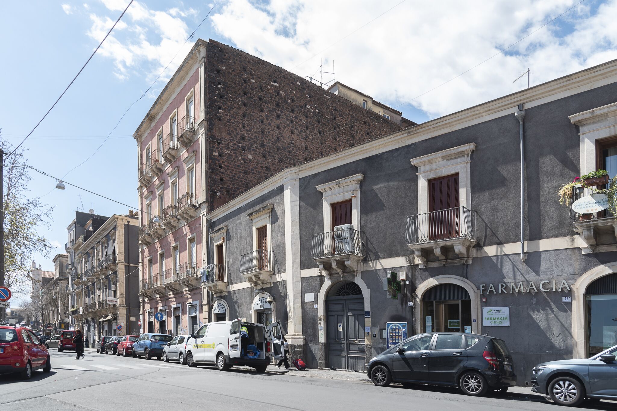 A street with parked cars and a pharmacy building with a sign reading "FARMACIA".