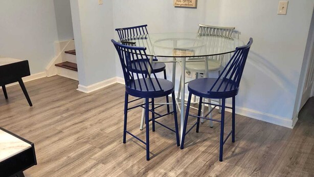 A dining area with a glass table and four blue chairs, a light fixture, and a wall with a list of house rules. - Cozy Treasure Home with private entrance (Buford)
