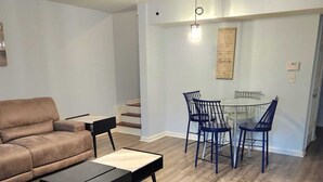 A living room with a brown leather couch, a black coffee table, and a dining area with blue chairs and a glass table. - Cozy Treasure Home with private entrance (Buford)