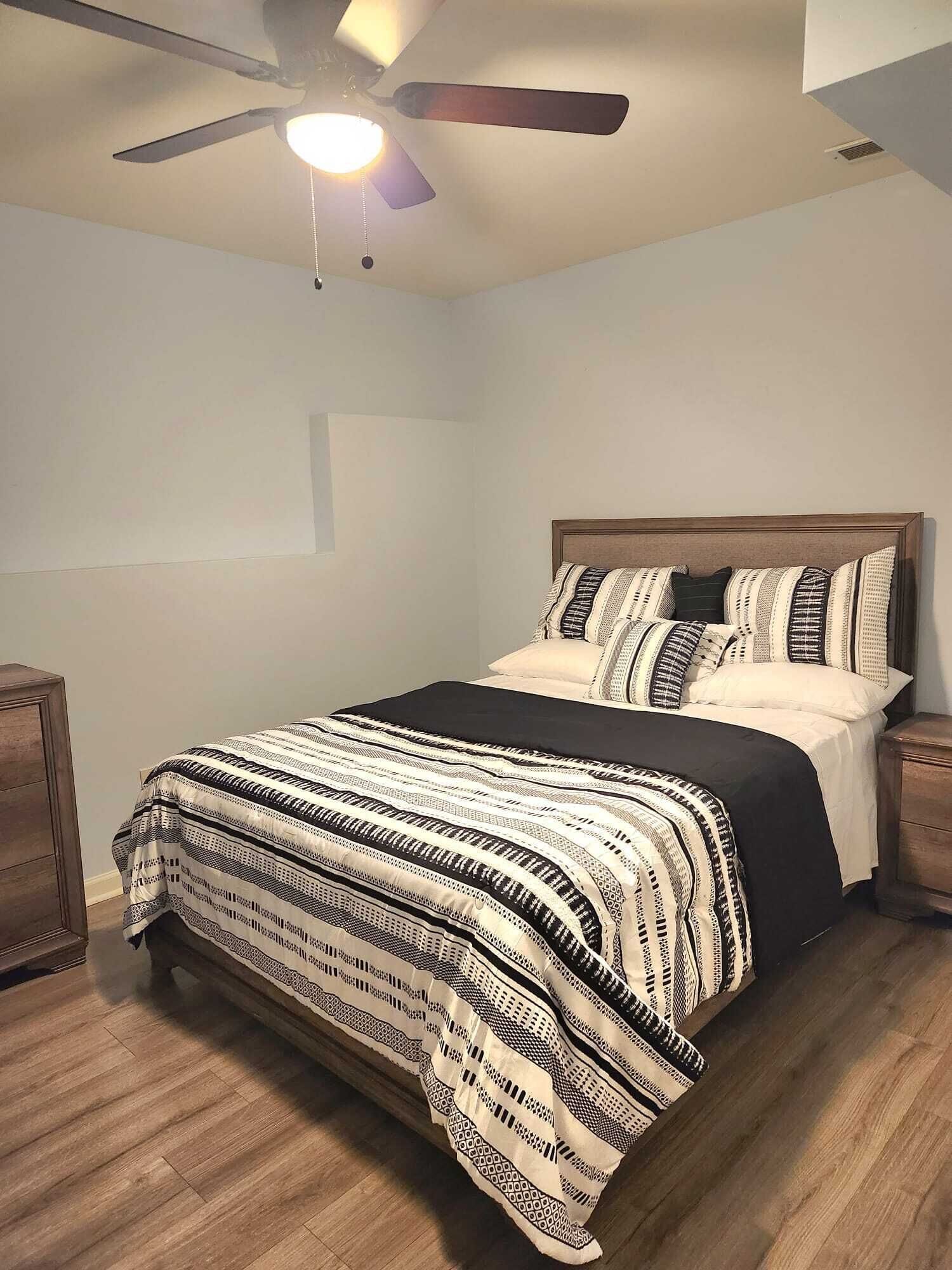 A bedroom with a bed, a ceiling fan, and wooden nightstands.