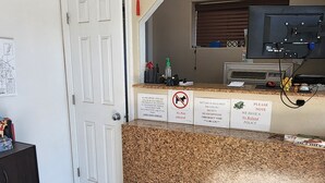 Un espace d’accueil d’hôtel avec un comptoir en granit, une porte fermée et un panneau indiquant qu’il est interdit d’y entrer avec des animaux.