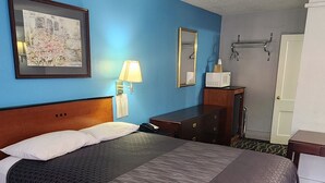 Une chambre d’hôtel avec un grand lit, une table de chevet, une commode, une lampe, un tableau encadré au mur et une porte.