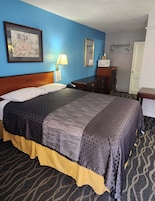 Habitación de hotel con una cama grande, una mesita de noche, un aparador, una lámpara, un cuadro enmarcado en la pared y una puerta.