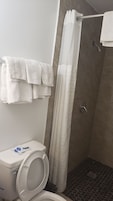 Un baño con inodoro, ducha con cortina y toallero con toallas.