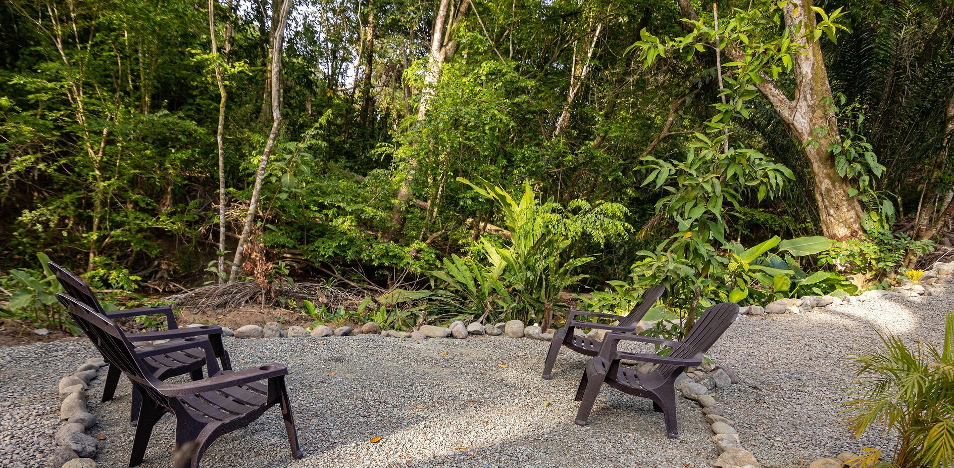 Un espace aménagé avec deux chaises et une table, entouré d’un chemin de gravier et d’une végétation luxuriante.