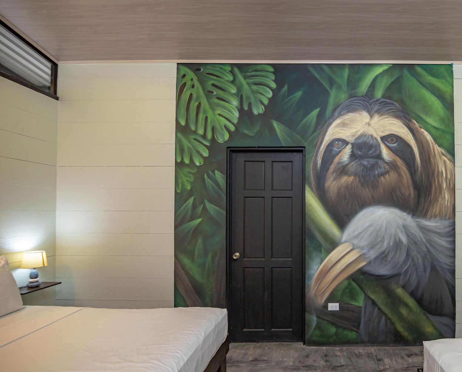 A room with a bed, a nightstand, a lamp, and a door.