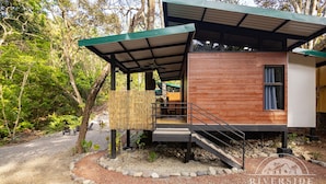 A modern bungalows with a covered outdoor area, wooden exterior, and a stone pathway. - Riverside Bungalows (Quepos)