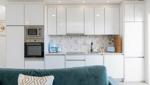 Een moderne keuken met witte kastjes, een magnetron, een oven en een koffiezetapparaat.