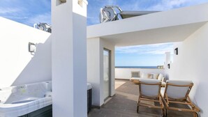 Een modern terras buiten met een bubbelbad, een zithoek met twee stoelen, en uitzicht op de zee.
