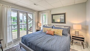 A bedroom with a large bed, two bedside lamps, a nightstand, and a view of a balcony. - True Lakefront, Easy Water Access, Dock, Hot Tub, Sleeps 12 (Penhook)