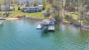 A lakeside property with a dock, a covered boat house, and a large house with a porch. - True Lakefront, Easy Water Access, Dock, Hot Tub, Sleeps 12 (Penhook)