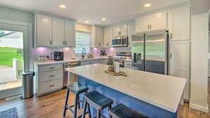 A modern kitchen with white cabinets, stainless steel appliances, and a large island with bar stools. - True Lakefront, Easy Water Access, Dock, Hot Tub, Sleeps 12 (Penhook)