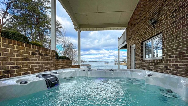 An outdoor hot tub area with a brick wall and a view of the sky and trees. - True Lakefront, Easy Water Access, Dock, Hot Tub, Sleeps 12 (Penhook)