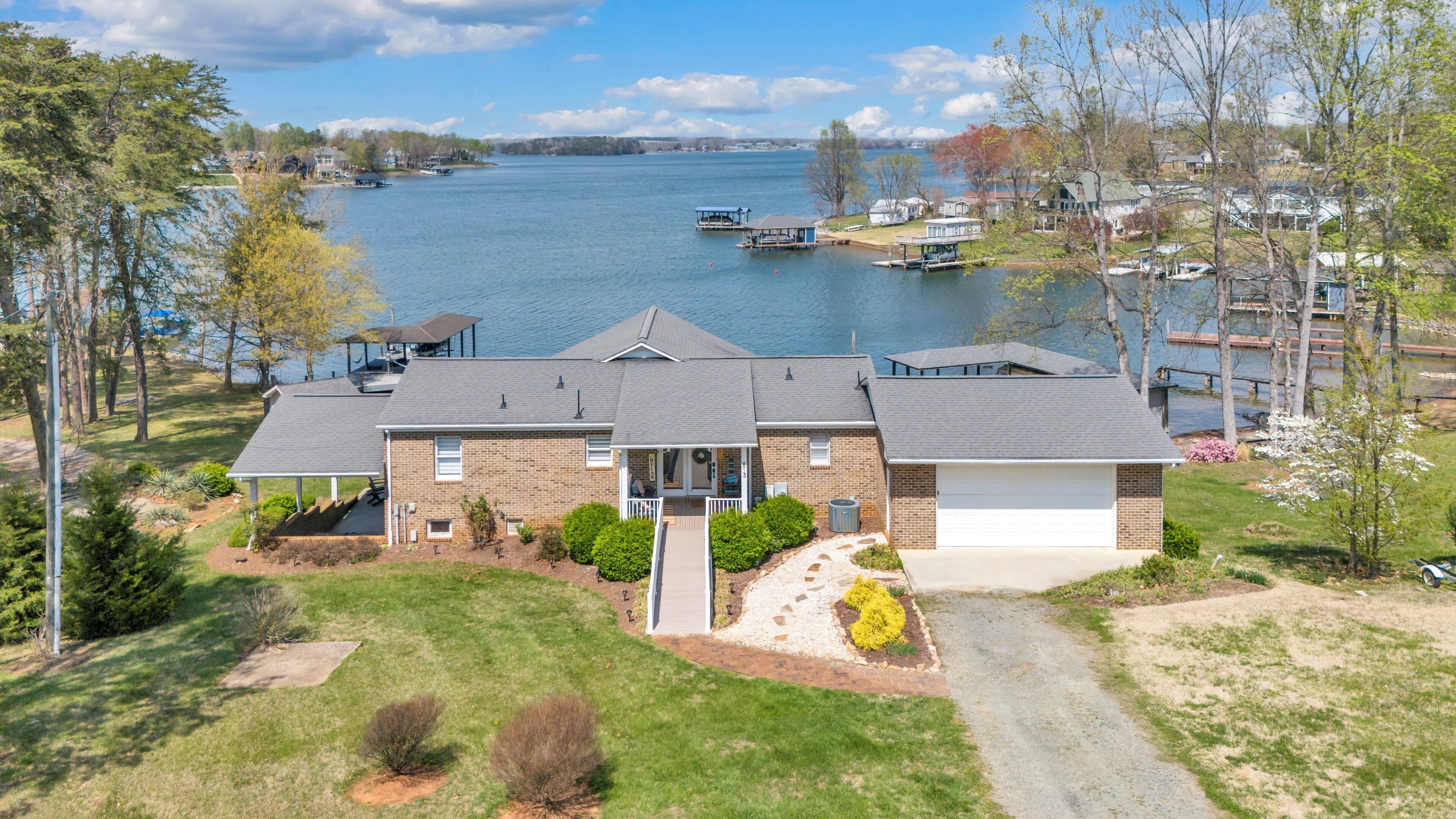 Une maison à deux étages dotée d’un porche abrité, d’un garage et offrant une vue sur un lac où naviguent des bateaux.