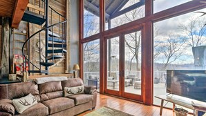 A cozy living room with a brown leather sofa, a spiral staircase, and a large sliding glass door leading to an outdoor patio.