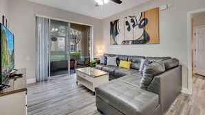 A modern living room with a grey leather sofa, a coffee table, and a ceiling fan. - Sunset view next to Waterpark/Pool. Moana, Beauty&Beast, etc. theme Near Disney. (Kissimmee)