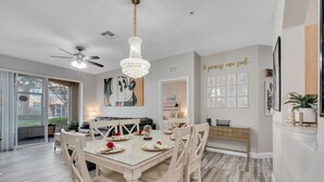 A dining area with a glass table, white chairs, and a chandelier. - Sunset view next to Waterpark/Pool. Moana, Beauty&Beast, etc. theme Near Disney. (Kissimmee)
