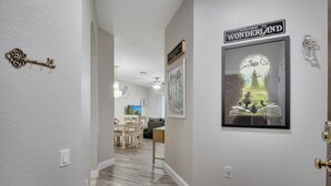 A hallway with a framed picture of a castle, a key on the wall, and a sign that reads "Welcome to Wonderland". - Sunset view next to Waterpark/Pool. Moana, Beauty&Beast, etc. theme Near Disney. (Kissimmee)