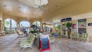 An outdoor patio area with seating, a Coca-Cola sign, and a sign for The Market Place & Grill. - Sunset view next to Waterpark/Pool. Moana, Beauty&Beast, etc. theme Near Disney. (Kissimmee)