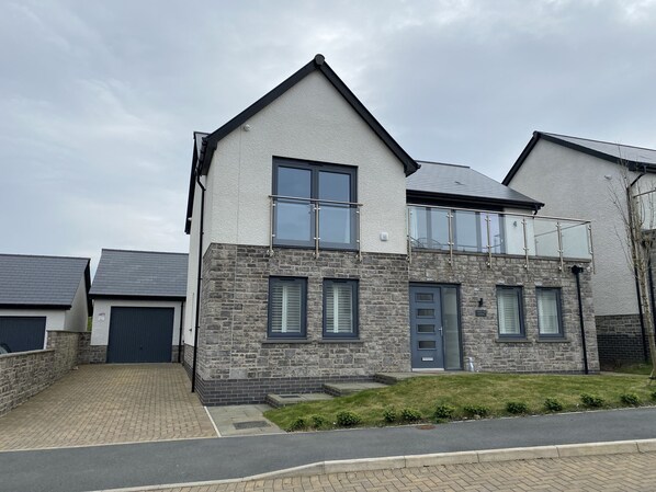 A two-story house with a stone facade, a grey door, and a balcony with glass railings. - Galwad y Mor (Haverfordwest)