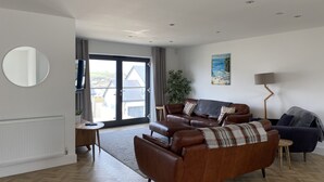 A modern living room with a brown leather sofa, a round mirror, and a painting on the wall. - Galwad y Mor (Haverfordwest)