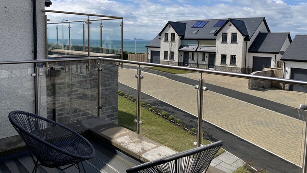 A balcony with a glass railing overlooking a street with houses and a clear sky. - Galwad y Mor (Haverfordwest)
