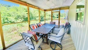 Un patio techado al aire libre con mesa y sillas de madera, rodeado de amplias ventanas con vistas a la vegetación.