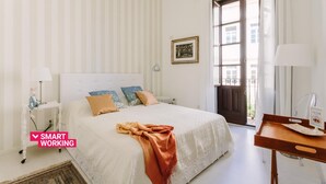 A neatly arranged bedroom with a bed, bedside tables, a desk, and a window. - Suite La Piazza by Wonderful Italy (Syracuse)