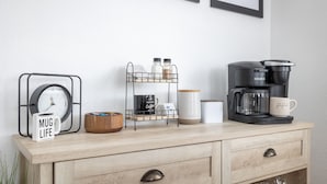 Une commode en bois avec une horloge, une tasse, une machine à café et un porte-épices.