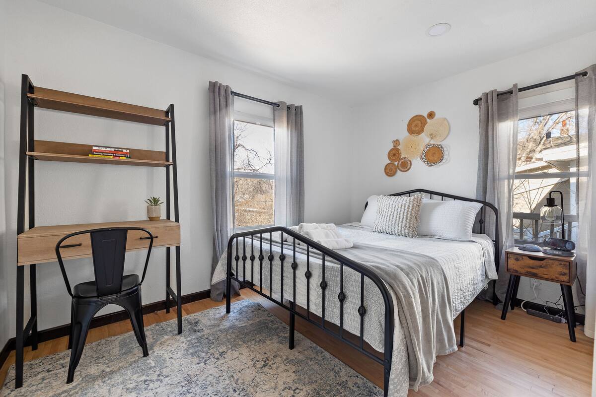 Un dormitorio con una cama, un escritorio con silla, una ventana con cortinas y decoración en la pared.