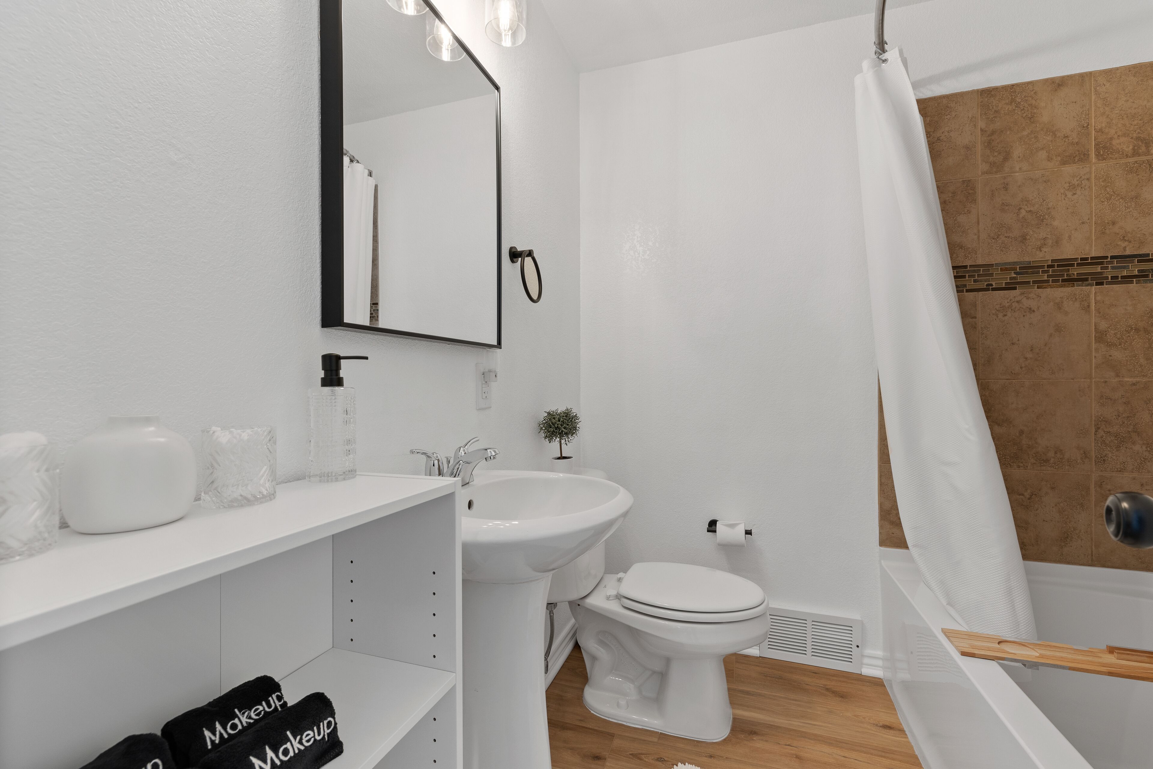 A modern bathroom with a white sink, vanity, and toilet. There is a shower curtain and a small potted plant on the vanity.