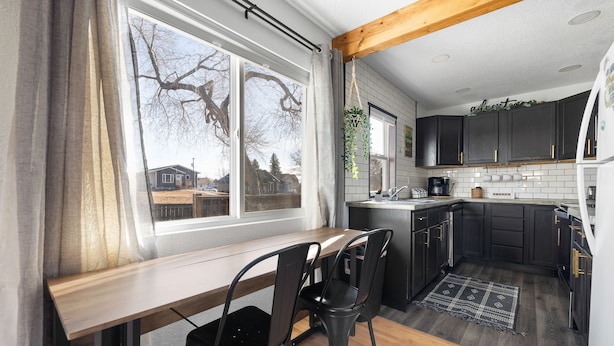 Une cuisine avec des meubles de couleur sombre, un plan de travail en bois et une fenêtre donnant sur une maison.