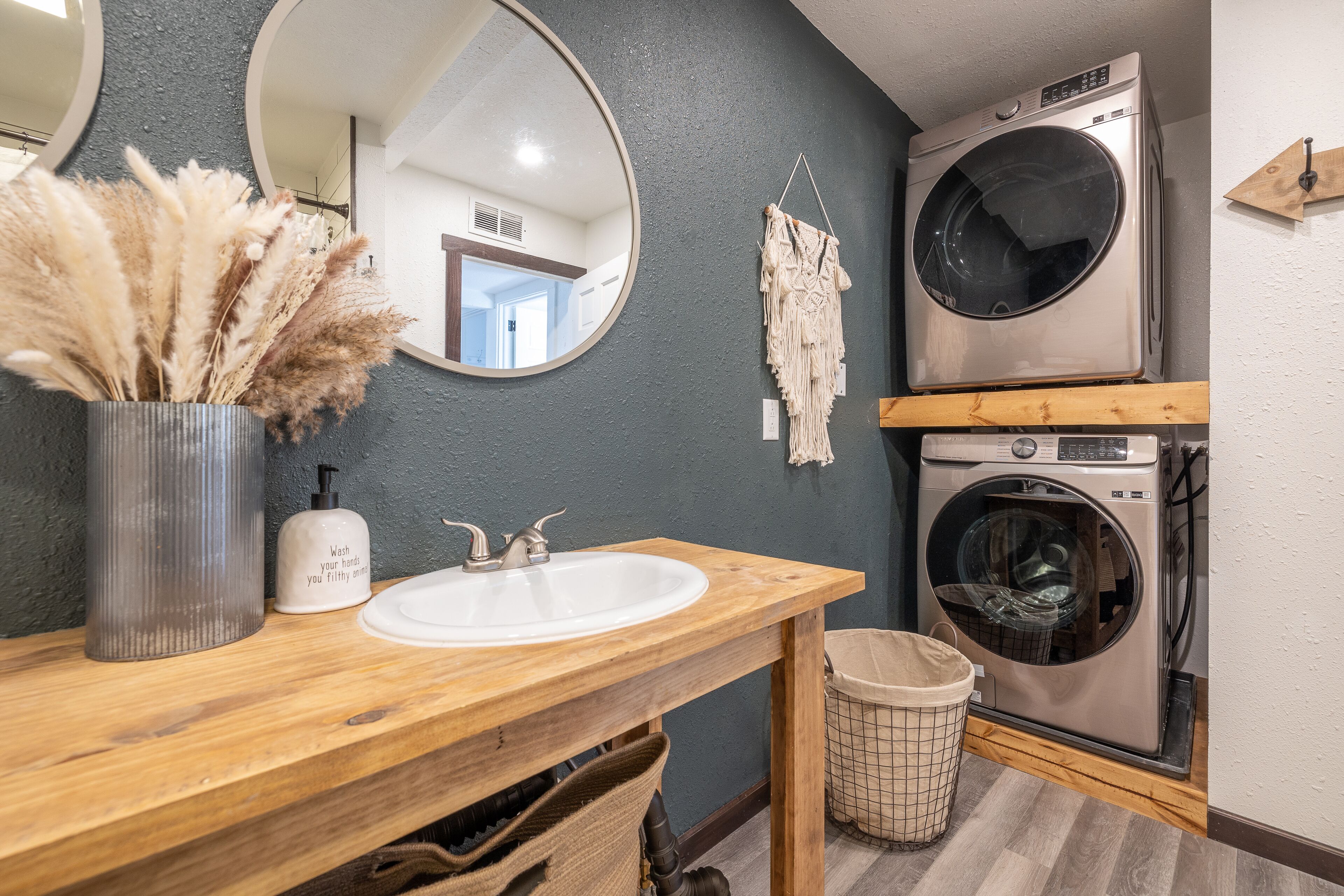 Un baño con tocador de madera, lavabo, espejo, lavadora y cubo de basura.