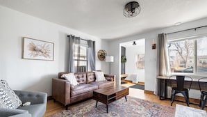 Un salon moderne avec un canapé en cuir marron, un fauteuil gris, une table basse en bois et un tapis à motifs.
