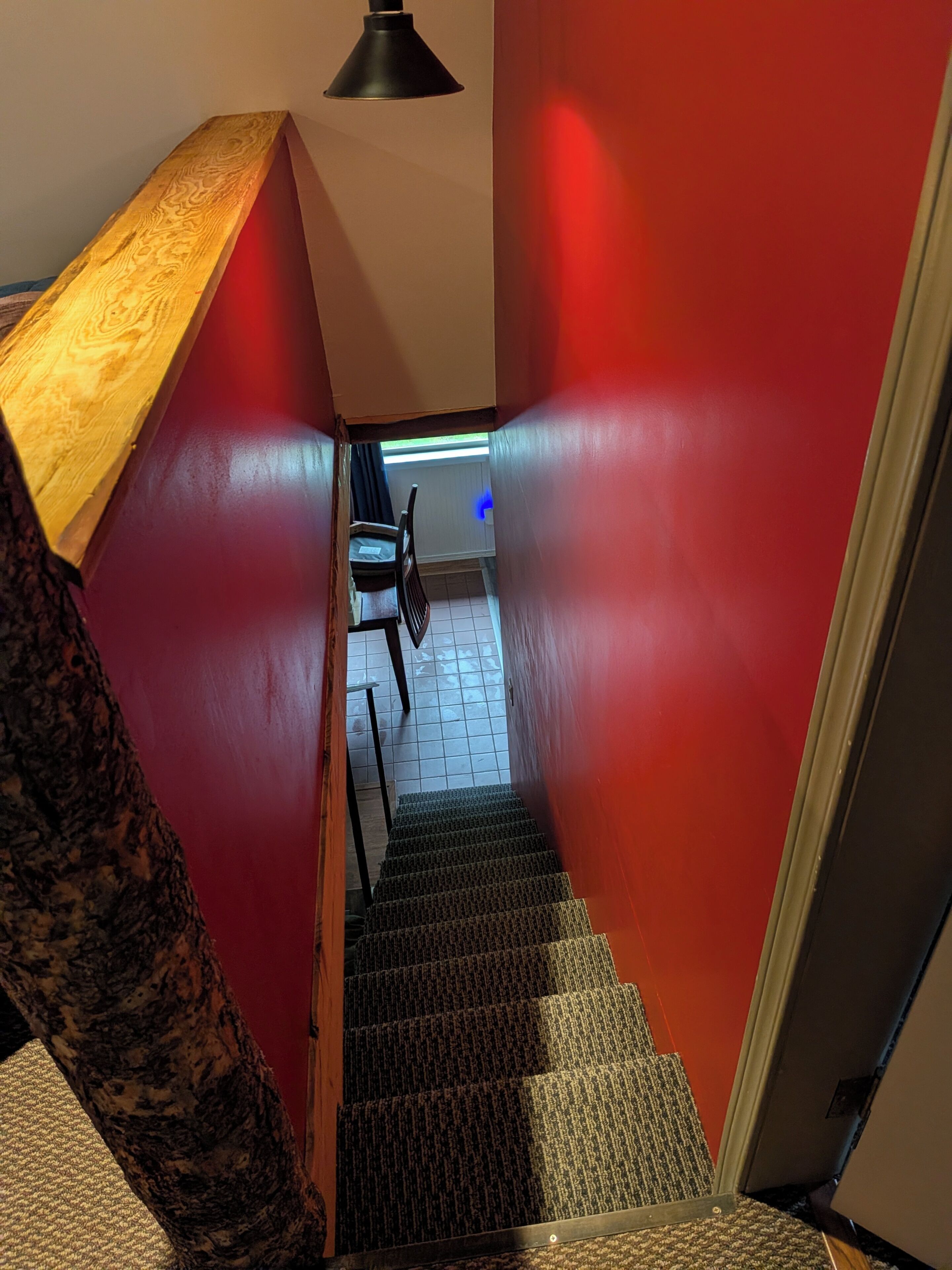 A staircase with red walls and a wooden handrail leading to a room with a desk and chair.