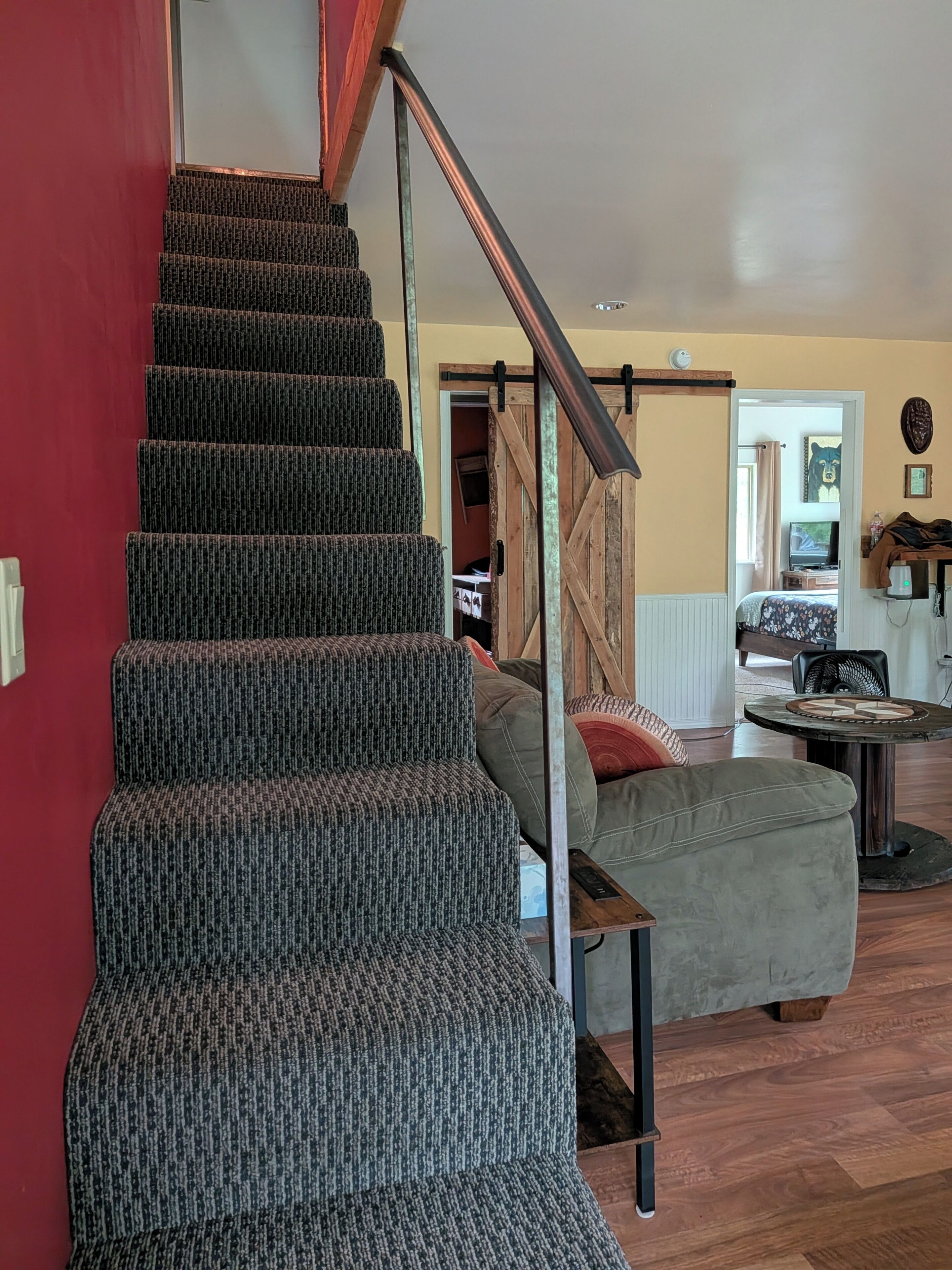 Un escalier avec une rampe métallique, un canapé gris et un plancher en bois.