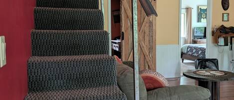 Un escalier avec une rampe métallique, un canapé gris et un plancher en bois.
