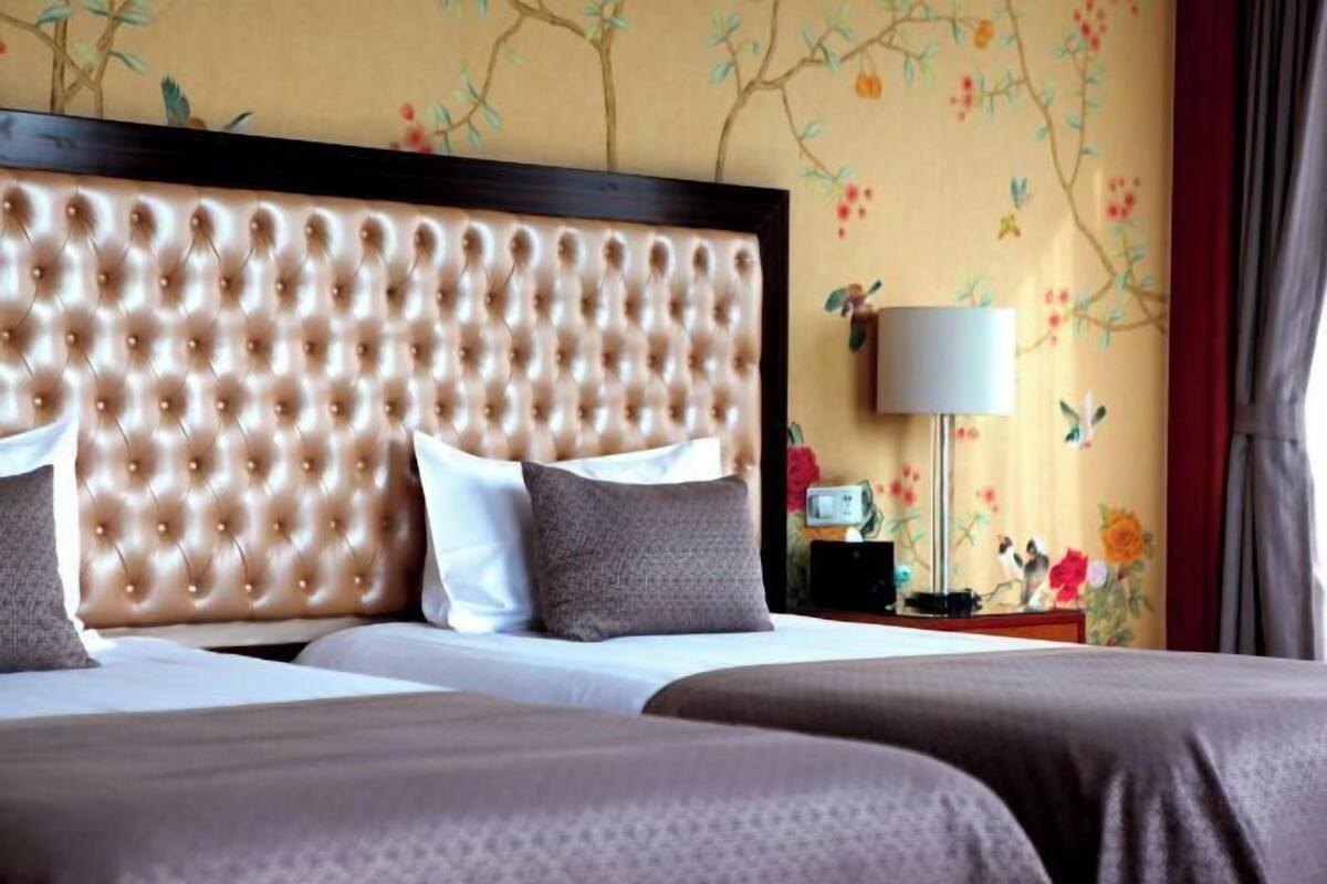A hotel room with a tufted headboard, a nightstand with a lamp, and floral wallpaper.
