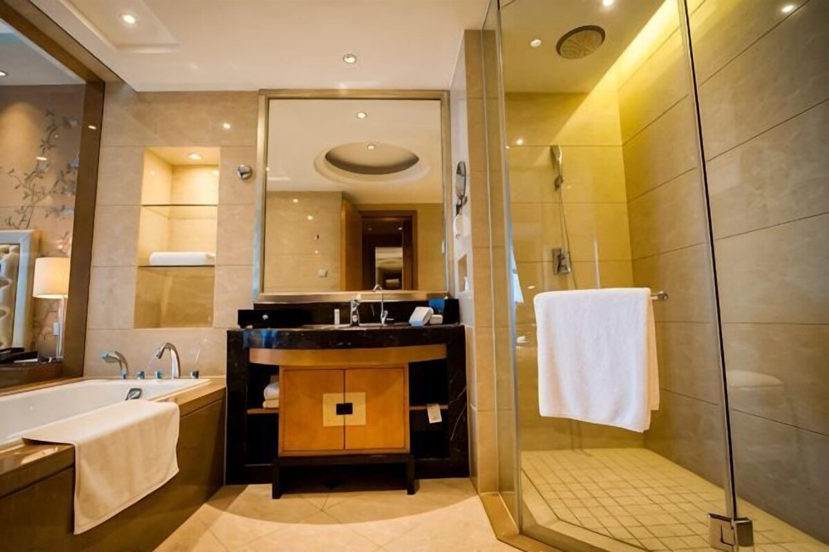 A modern bathroom with a large mirror, a bathtub, a shower, and a vanity with a towel.