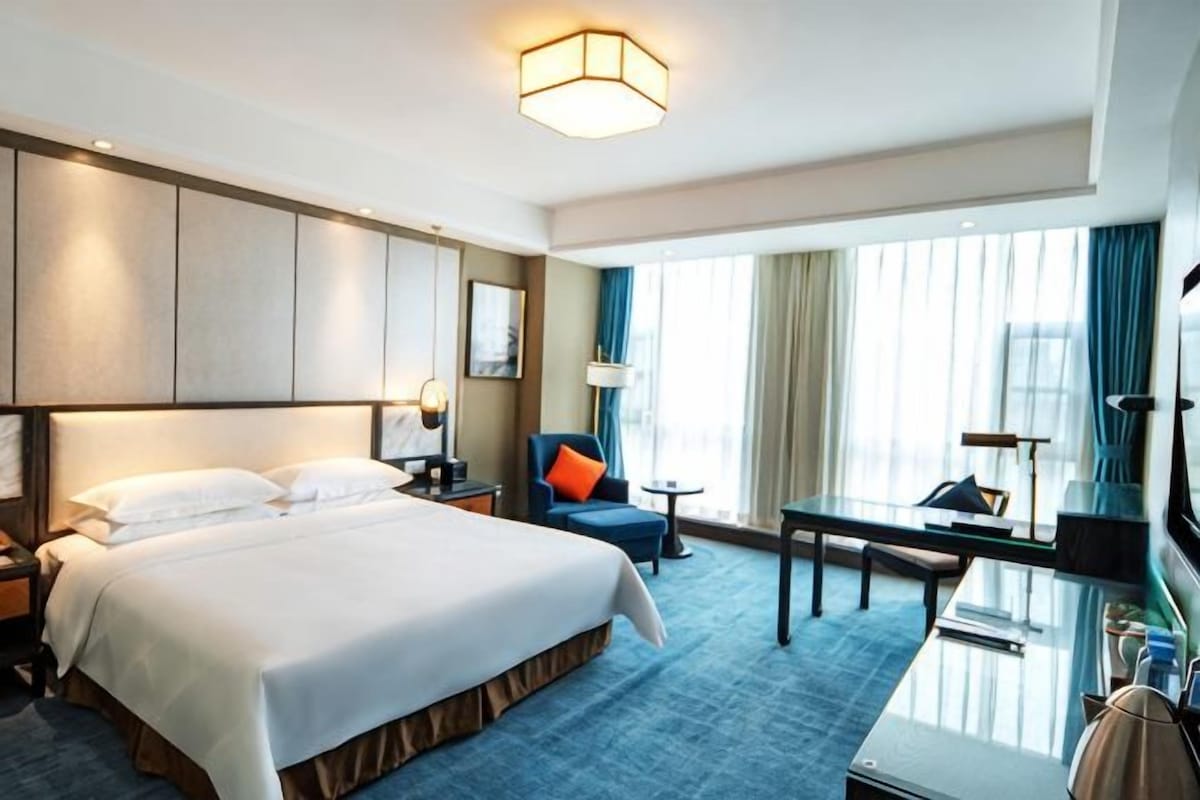 A hotel room with a large bed, a desk, a chair, and a TV.