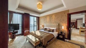 Habitación de hotel con una cama grande, televisión, un banco y vista al vestíbulo.
