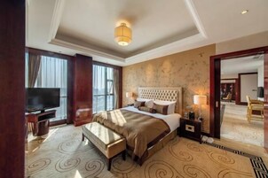 Ett hotellrum med en stor säng, en tv, en bänk och utsikt över lobbyn.
