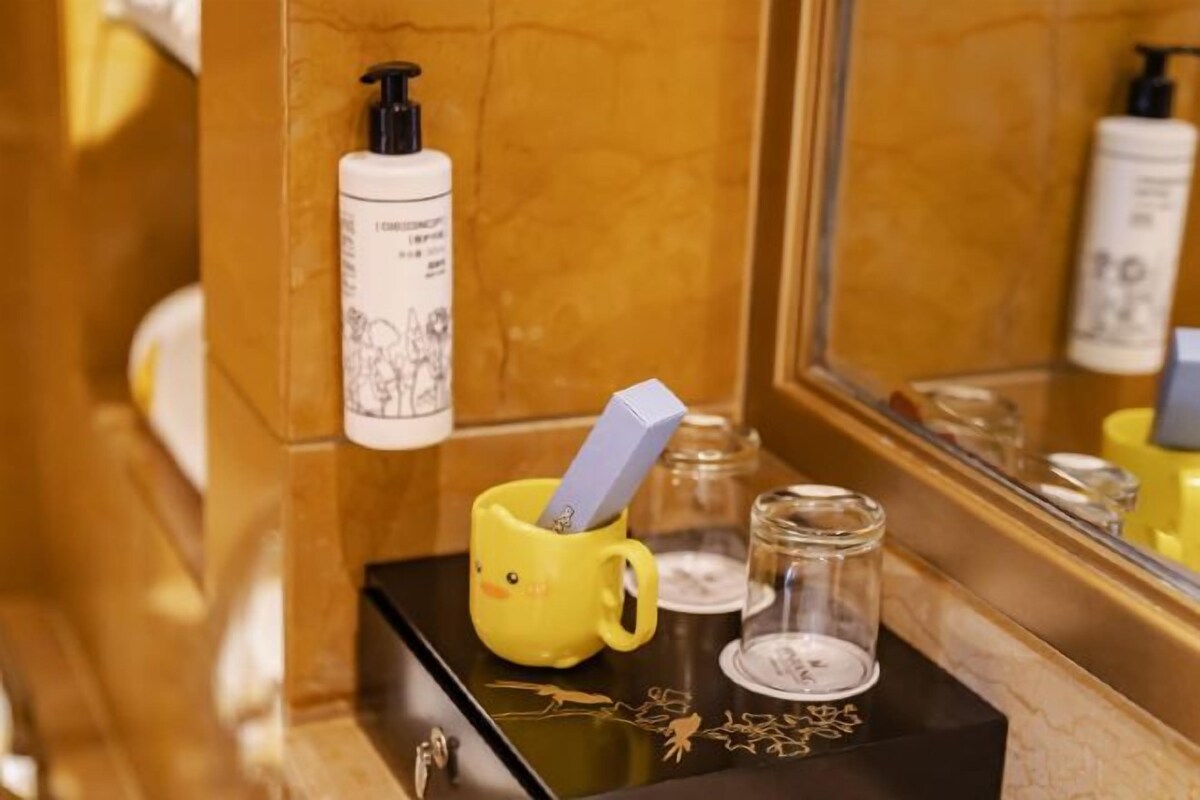 A bathroom vanity with a yellow mug, a bottle of shampoo, and a mirror.