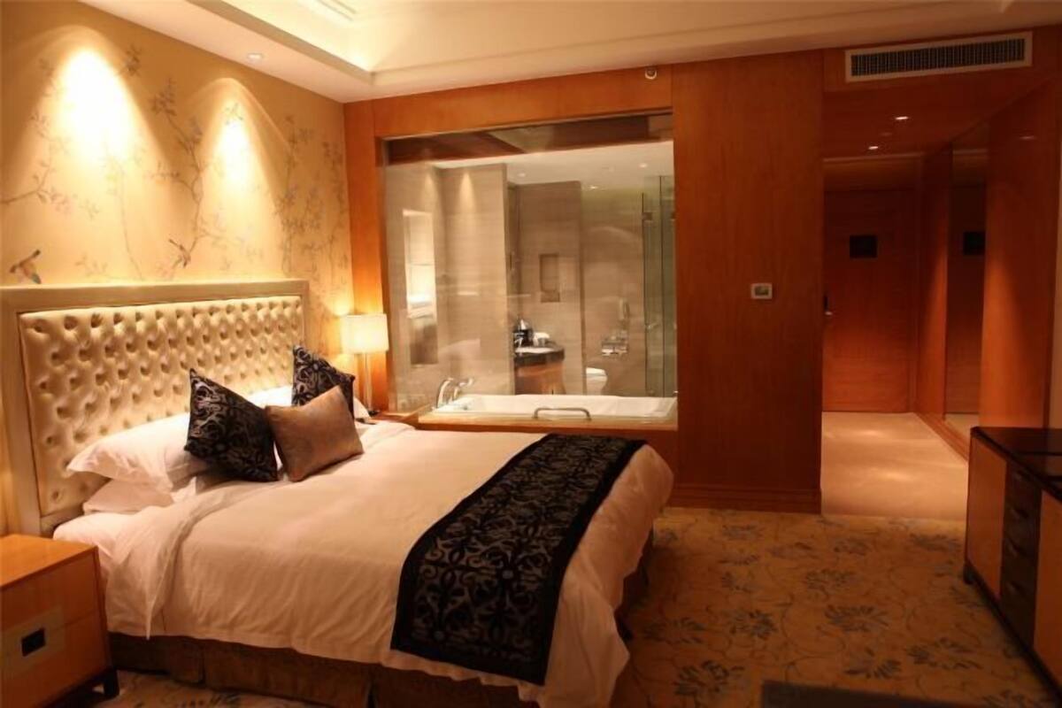 A hotel room with a large bed, a glass-enclosed bathroom, and a wooden floor.