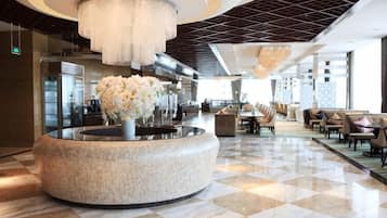 A hotel lobby with a round marble reception desk, a large chandelier, and a check-in counter.